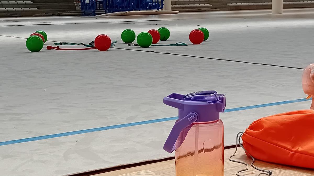 Botella de agua de una niña y, al fondo, las cintas y pelotas en el suelo del pabellón de San Vicente, en un descanso de los entrenos