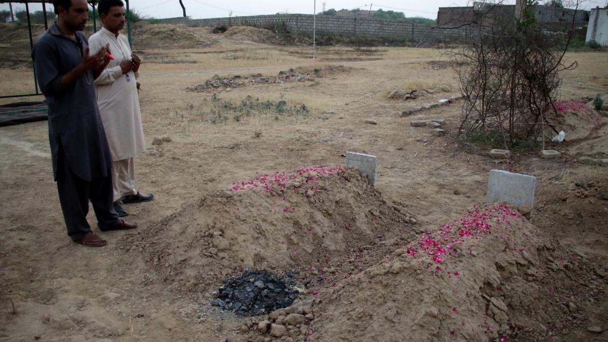 Dos homes preguen davant les tombes de les dues dones assassinades al Pakistan. | EFE