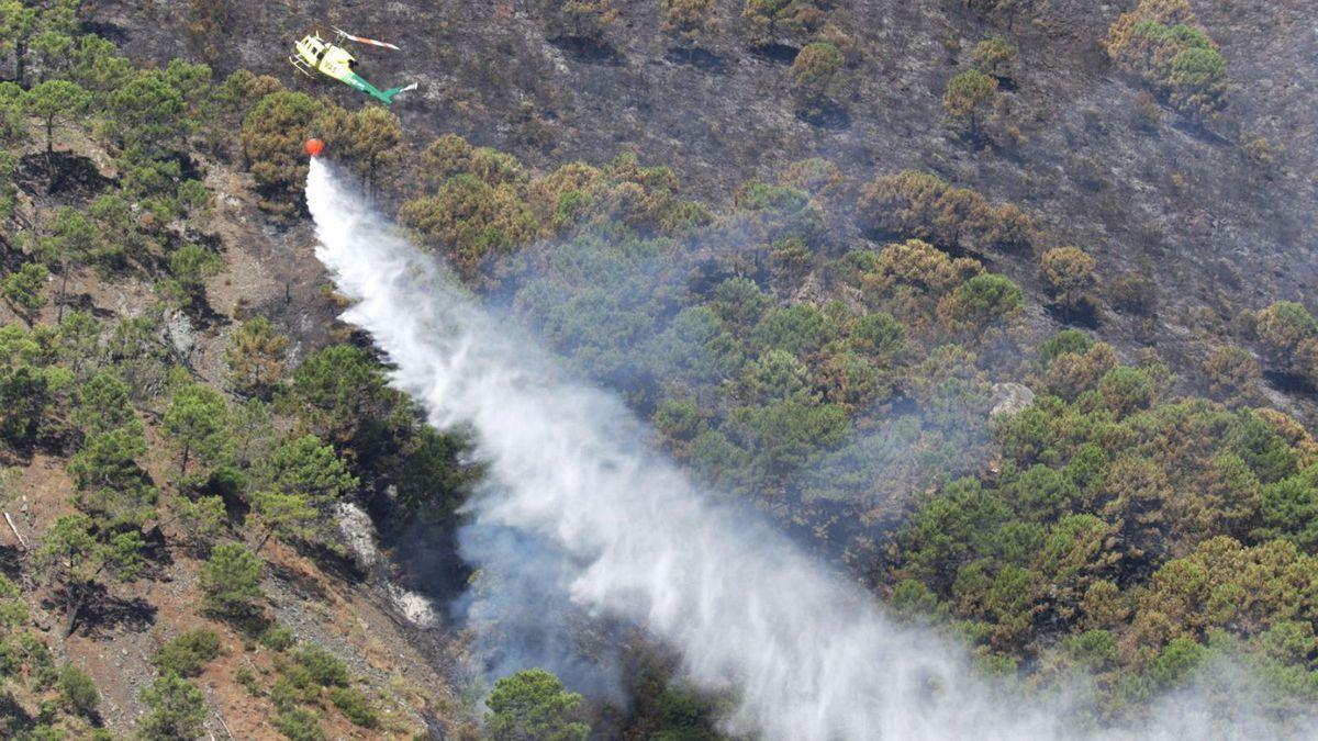 Un helicóptero lanza agua sobre el terreno afectado por el fuego.