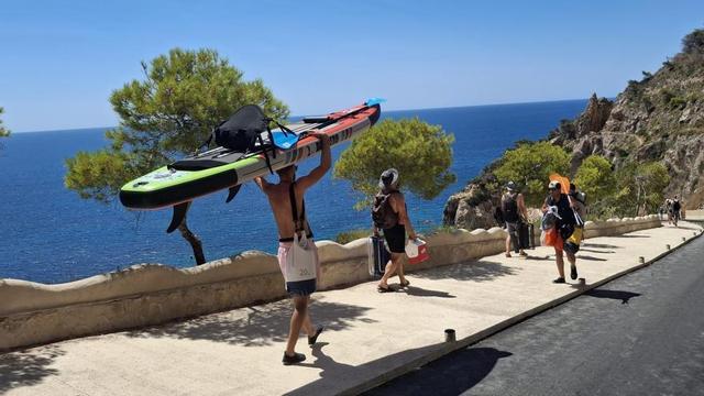 Un joven carga una tabla de pádel surf en la bajada a la cala del Moraig de Benitatxell. | A. P. F.