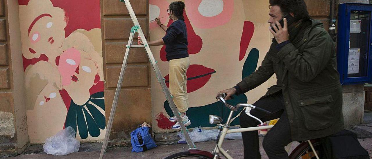 Un ciclista pasa por la calle Magdalena mientras Inés Iglesias pinta su mural.