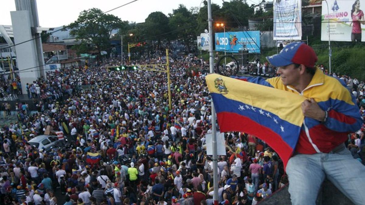 Un simpatizante de la oposición ondea una bandera venezolana ante cientos de personas congregadas para celebrar los resultados electorales en Venezuela.