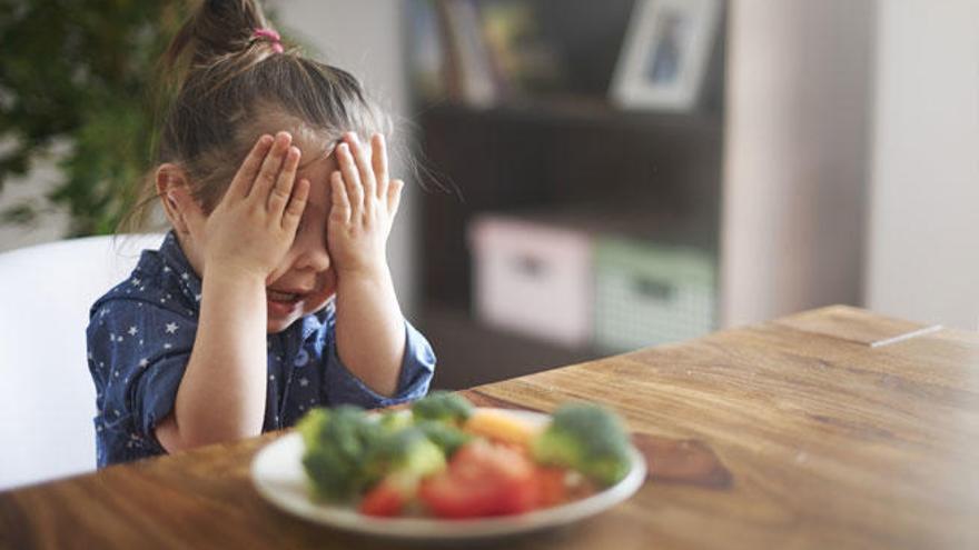 Una niña, ante un plato de verduras.