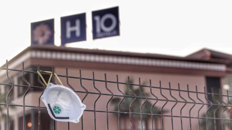 Una mascarilla cuelga de una de las verjas que separa la calle del hotel del sur que estuvo en cuarentena.