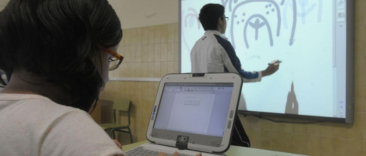 Dos alumnos trabajan en un aula con el ordenador y con la pizarra digital. | V. E.