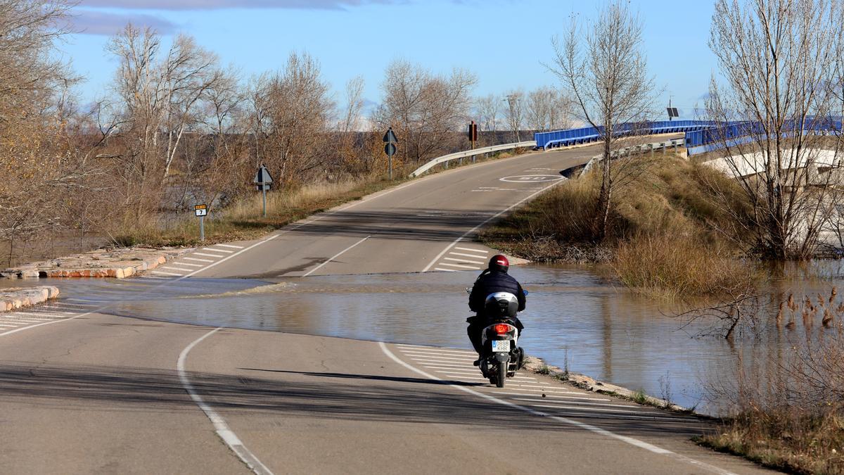 Un vecino de Pradilla se acerca en moto a contemplar el agua del río sobre la carretera.