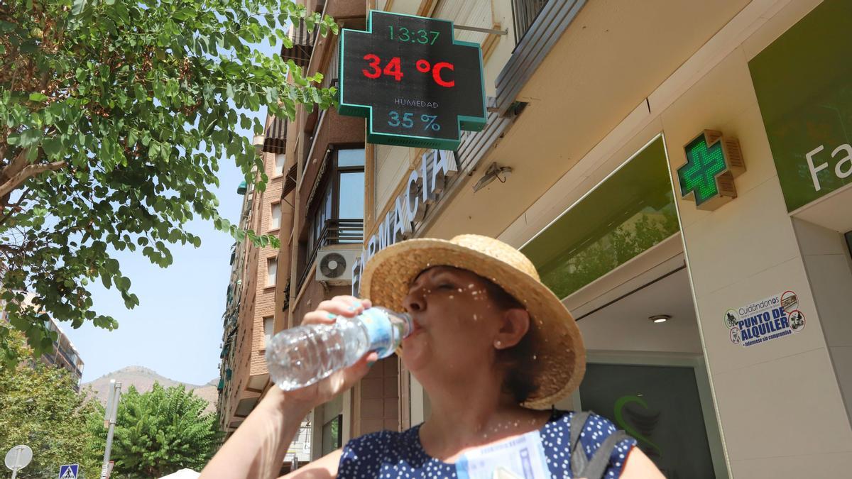 Una mujer bebe agua frente a una farmacia de Orihuela.