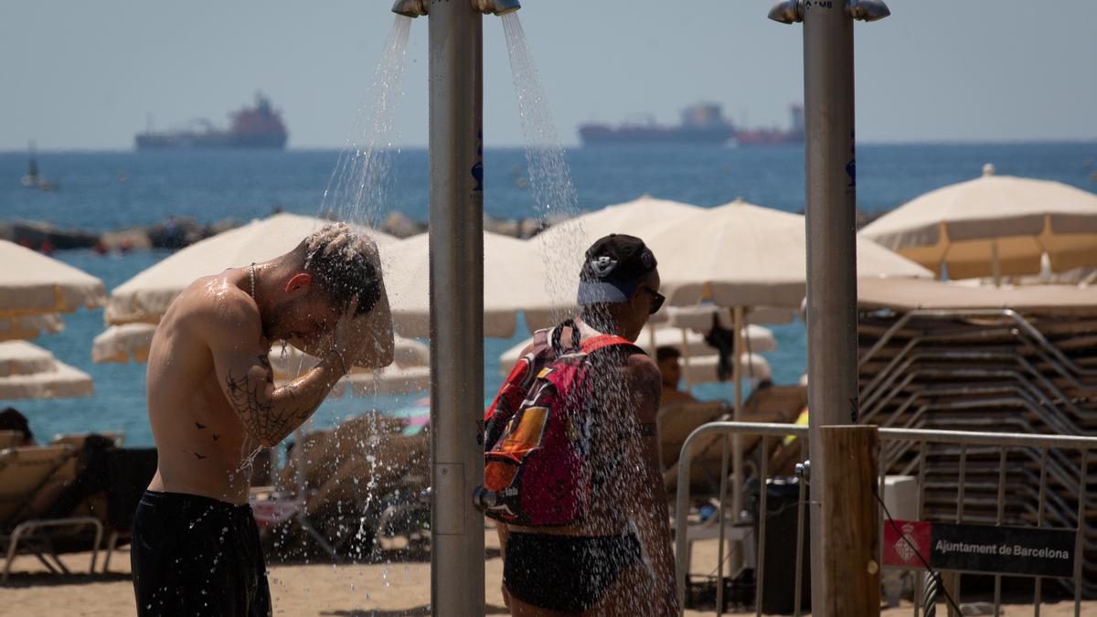 Varias personas se mojan en las duchas de la playa de la Barceloneta, a 13 de julio de 2022, en Barcelona, Catalunya (España). La intensa y extensa ola de calor llega hoy a su momento cumbre, aunque ese pico se mantendrá durante varios días seguidos, segú