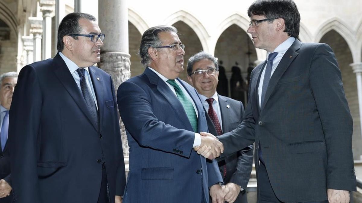 El presidente de la Generalitat, Carles Puigdemont, saluda al ministro del Interior, Juan Ignacio Zoido, ante el 'conseller' de Interior, Jordi Jané, este lunes, 10 de julio, antes del comienzo de la reunión de la Junta de Seguridad.