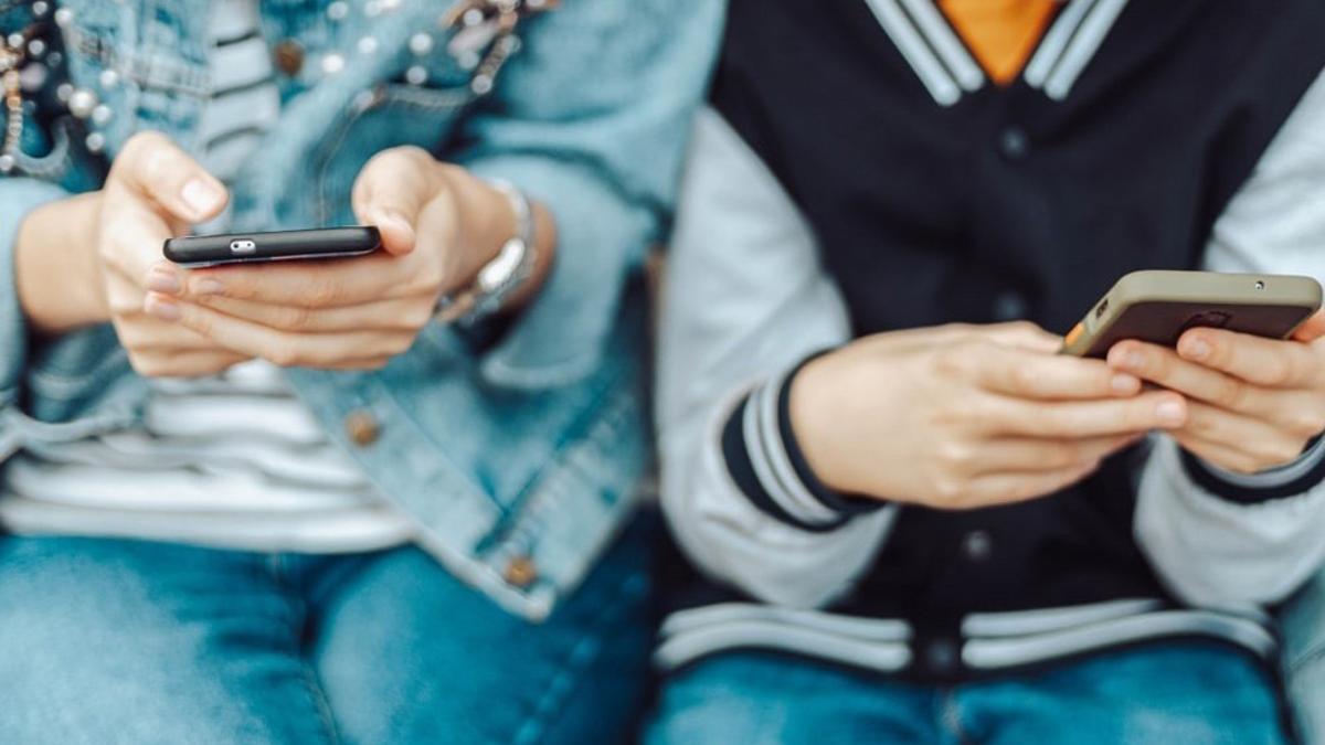 Dos jóvenes atentos a la pantalla de sus teléfonos móviles.