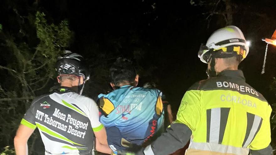 Un bombero ayuda al ciclista herido junto al compañero del deportista, tras acceder para su rescate al lugar donde había caído.