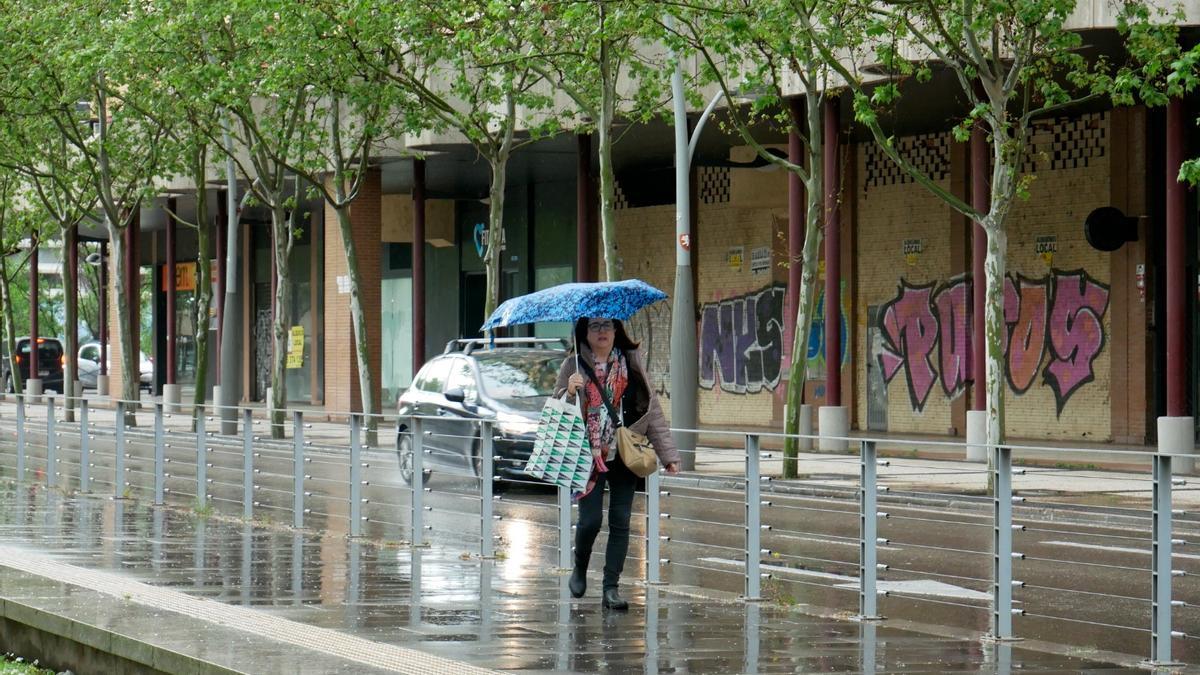 Una mujer camina bajo la lluvia este mediodía en Zaragoza.