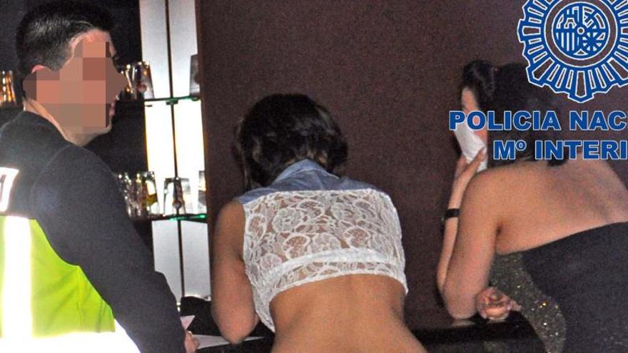 Dos de las mujeres del club, junto a un agente policial durante el arresto del dueño del local.