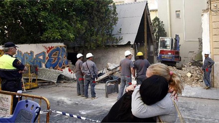 desesperación. Dos falleras se abrazan llorando al ver cómo la máquina excavadora derriba la parte trasera del que ha sido su casal-barraca durante treinta años.