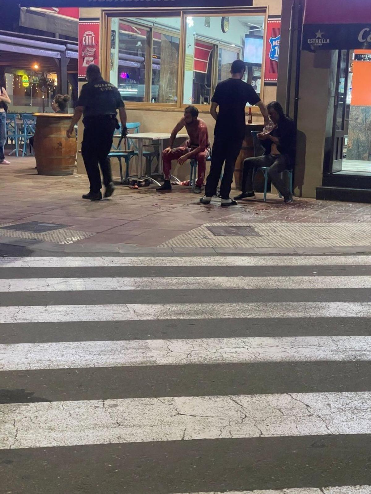 El hijo y el padre, heridos, sentados a la puerta del bar mientras esperaban a las ambulancias.