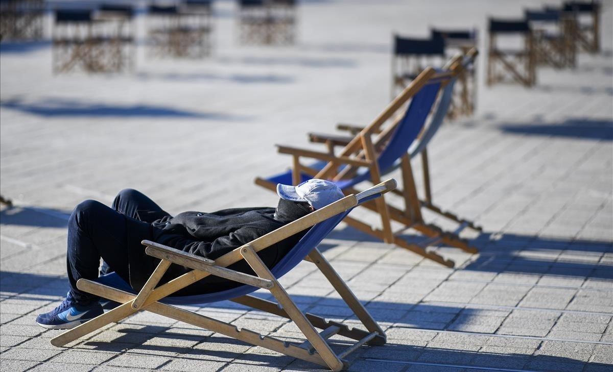 Un hombre toma el sol en la Plaza de les Glòries de Barcelona bien abrigado dado el descenso de temperaturas registrado por causa de la ola de frío.