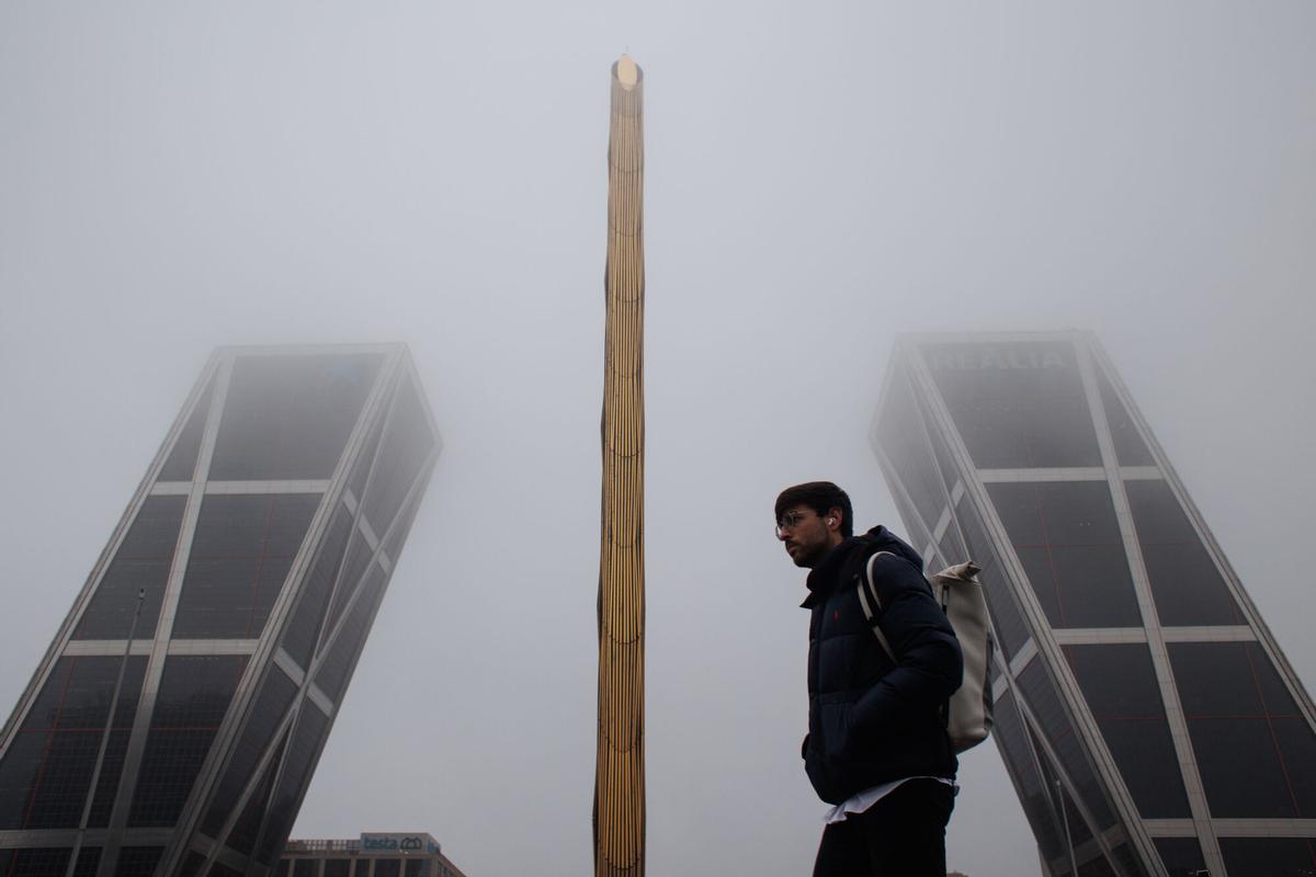 Un hombre pasa por delante de la Puerta de Europa o popularmente conocidas como 'Torres KIO' cubiertas de niebla.