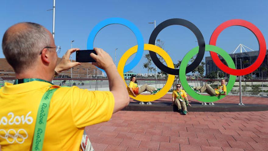 Varios voluntarios se fotografían junto a unos aros olímpicos en la villa. // Reuters