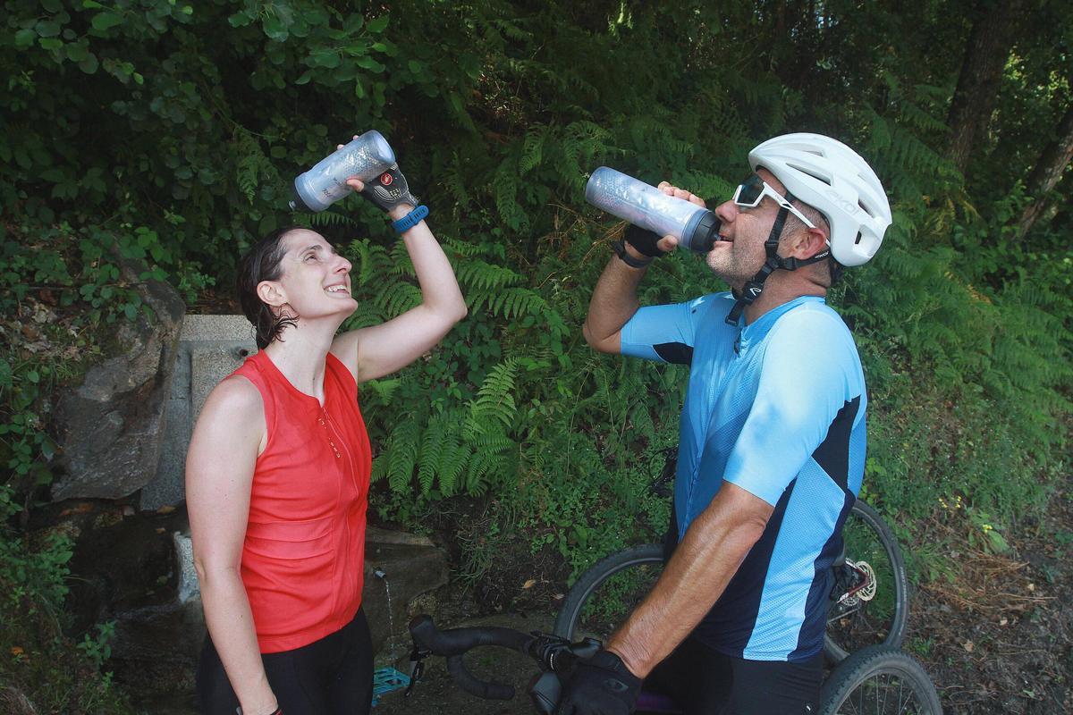 Dos ciclistas beben y se refrescan para aliviar el calor y mantener la hidratación, este domingo en Ourense.