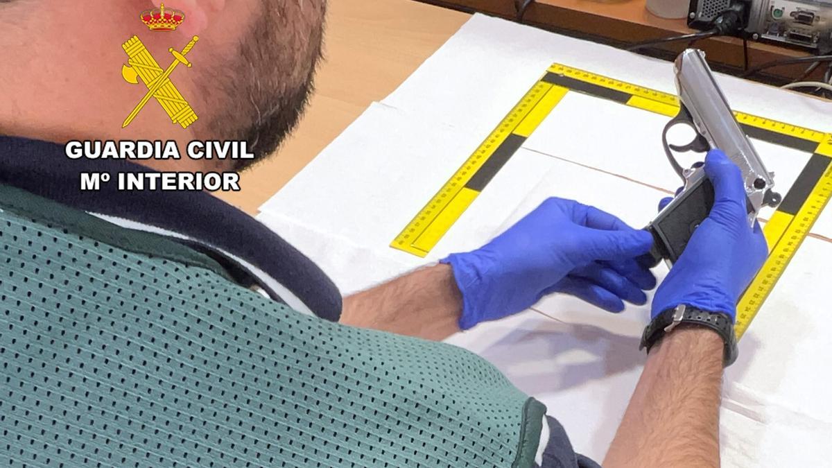 Un guardia civil sostiene la pistola intervenida a los detenidos.