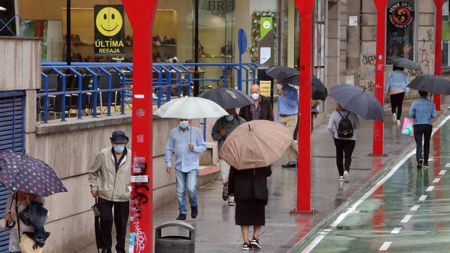 Los peatones circulan por López Mora, en el entorno de Praza América, en medio de una lluvia de verano.