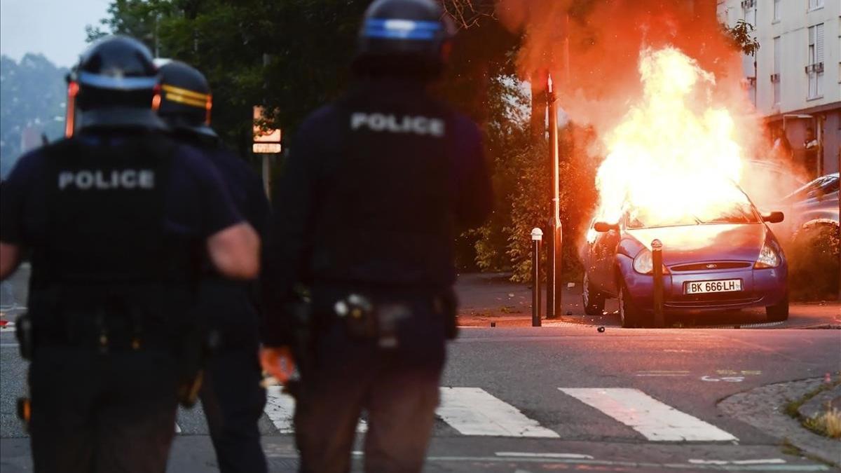 Varios policías ante un coche ardiendo, en Nantes.