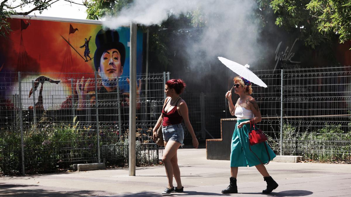 Unos turistas intentan refrescarse en unos vaporizadores de agua fresca instalados en los refugios climáticos del Passeig Joan de Borbó, en la Barceloneta.