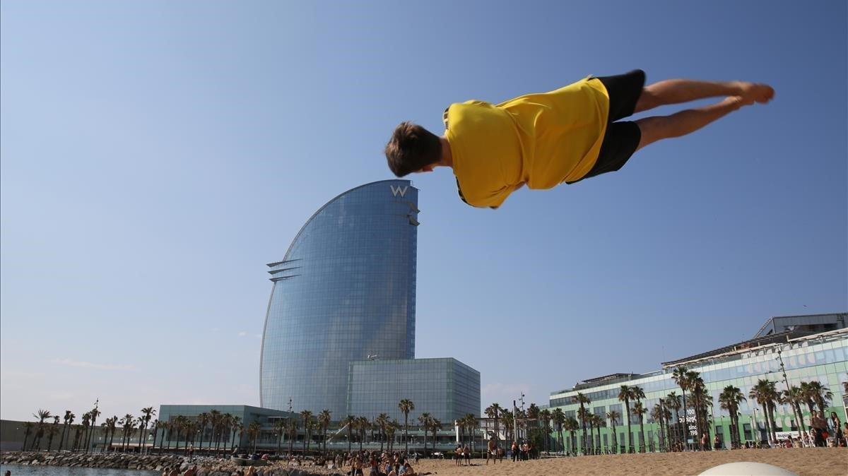 Un joven hace piruetas sobre la arena dela playa de Sant Sebastià, en la Barceloneta.