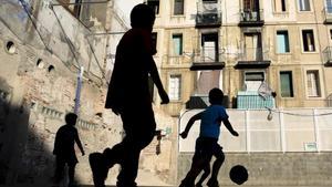 Varios niños juegan a fútbol en una pista del Raval, en Barcelona.