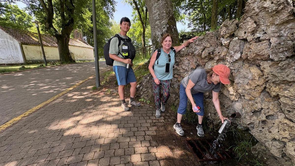 Por la izquierda, Daniel Wei, María Rosa Andújar y Paula Abejón rellenan sus cantimploras de agua fresca en la fuente de San Roque.