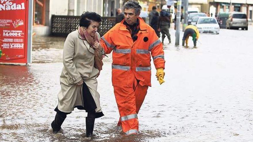 Un miembro de Protección Civil ayuda a una mujer a cruzar la inundada avenida de Ourense, en Cangas, donde el nivel de agua alcanzó una altura de medio metro  // Carmen Giménez