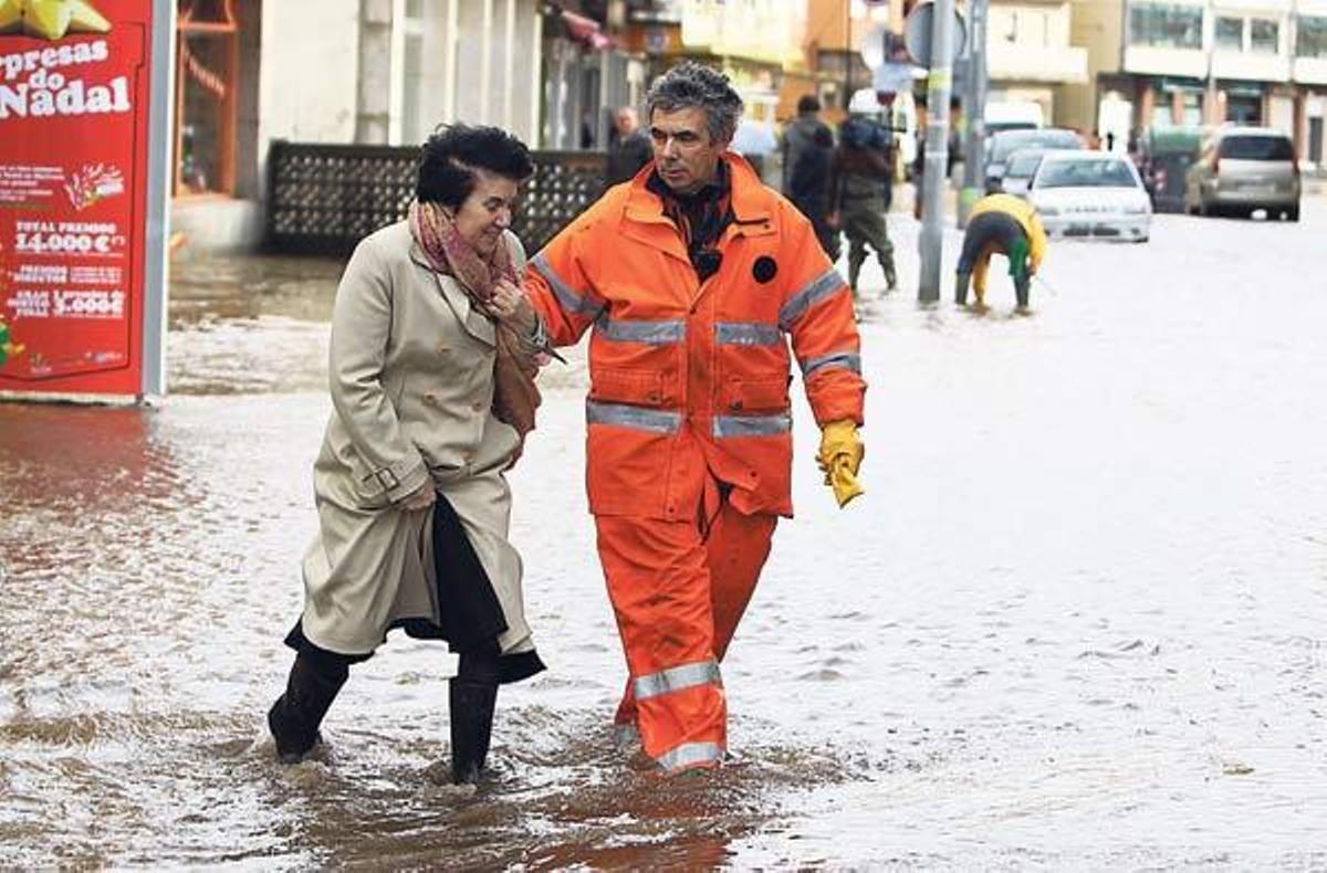 Un miembro de Protección Civil ayuda a una mujer a cruzar la inundada avenida de Ourense, en Cangas, donde el nivel de agua alcanzó una altura de medio metro // Carmen Giménez