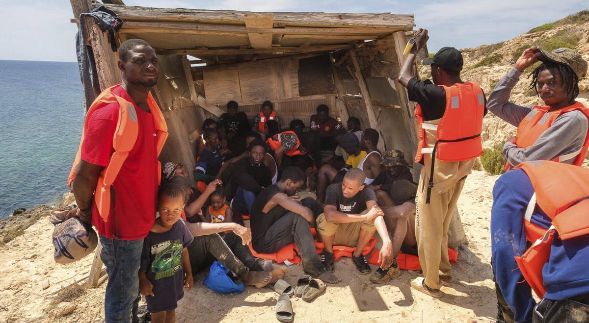 Los migrantes se cobijan en una sombra recién llegados en patera a la zona de s’Estufador, en Formentera. | JAVI PAREJO