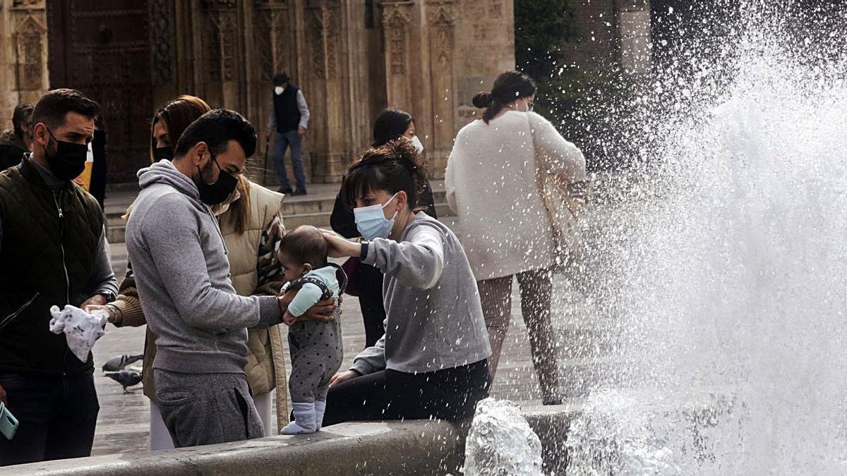 Una familia con mascarilla descansa en una fuente de la Plaza de la Virgen de València. | EDUARDO RIPOLL