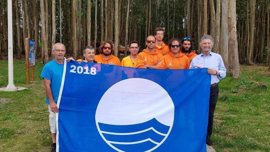 Marino Fernández, a la izquierda, e Ignacio García Palacios, a la derecha, junto al equipo de salvamento de Frexulfe, sosteniendo la bandera azul otorgada a este arenal.