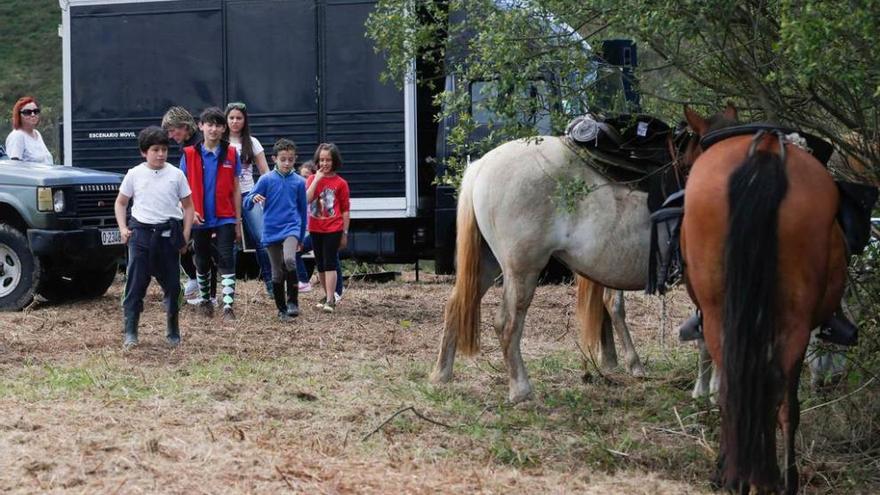 Unos niños observan unos caballos que descansan bajo un árbol.