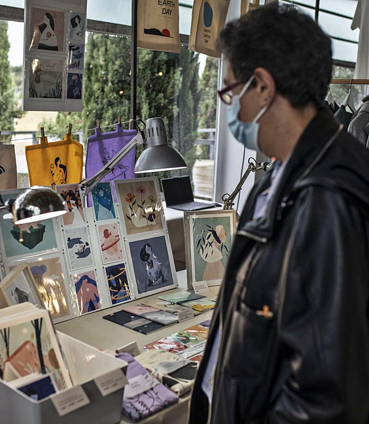 Un visitante observa la oferta de un puesto de ilustraciones. | Emilio Fraile