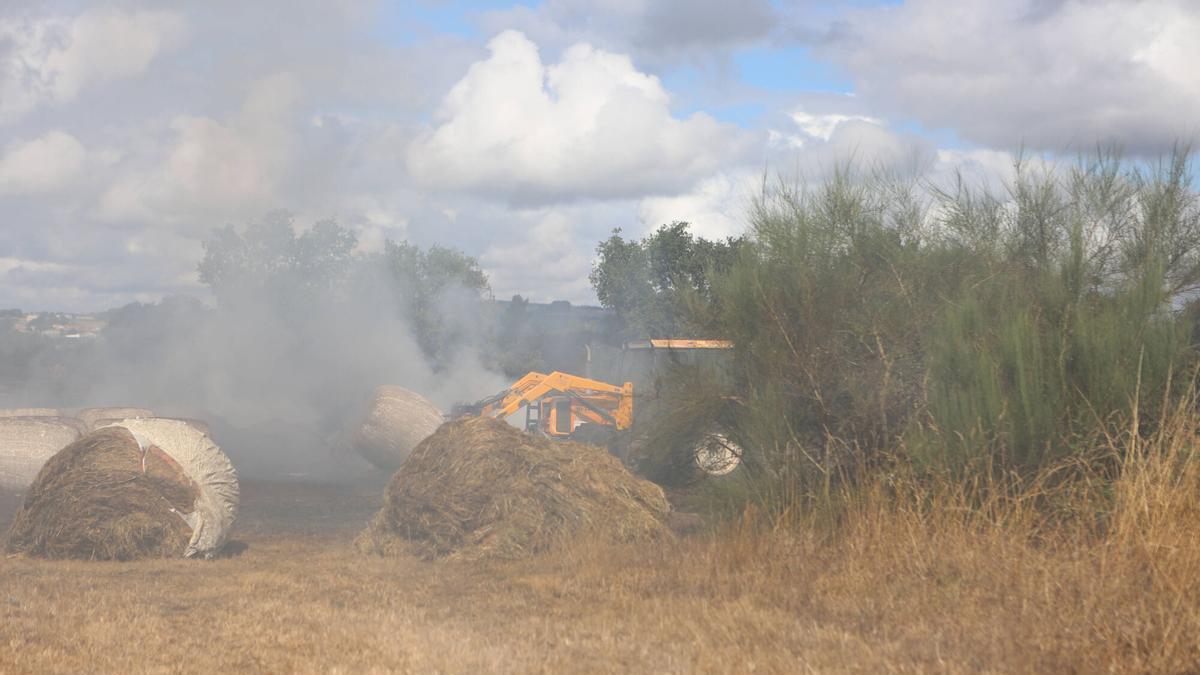 Un tractor retira silos de hierba quemados por el fuego de Carboentes.