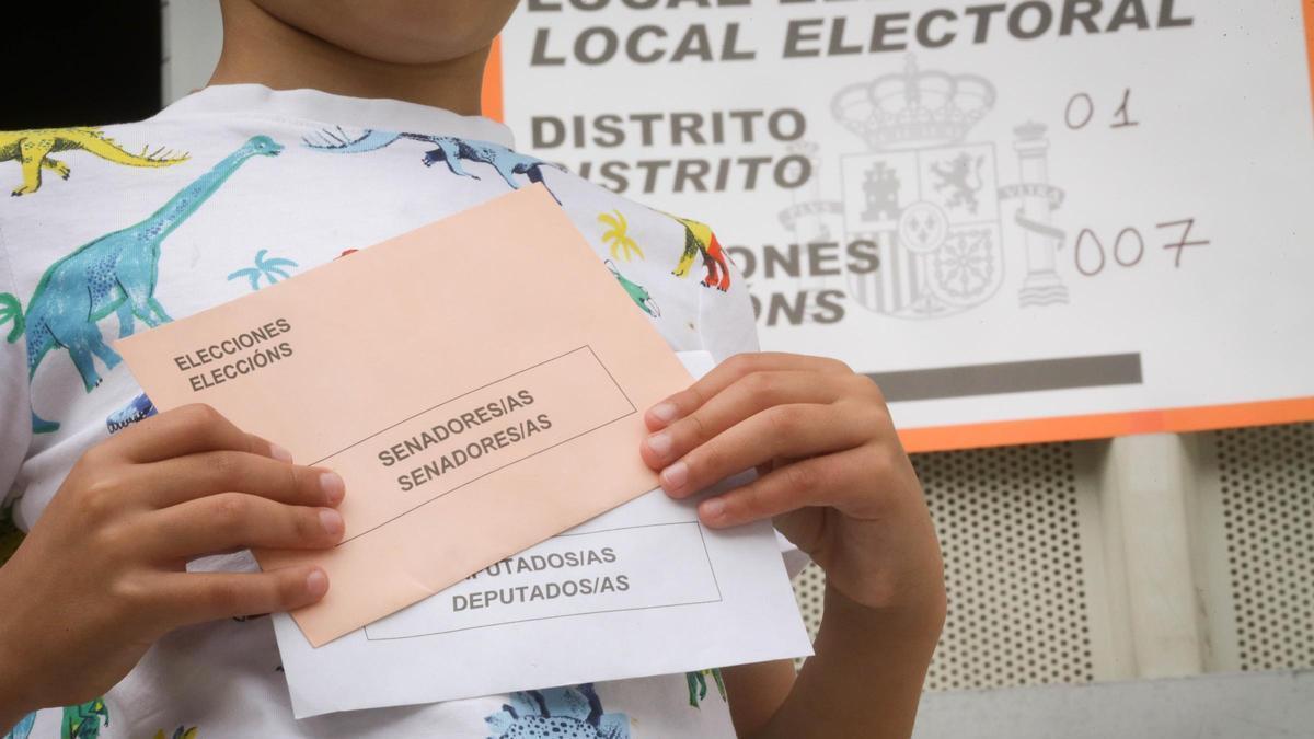 Un niño sostiene los dos sobres de las elecciones generales de 2023, en Foz (Lugo).