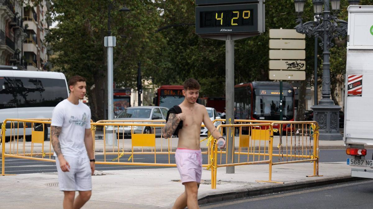 Dos jóvenes paseando el viernes pasado en València frente a un termómetro que marca 42 grados.