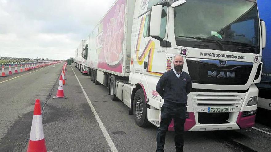 El transportista Juan Antonio Simón, junto a su camión, parado en Dover y con una larga fila de vehículos pesados detrás. | INFORMACIÓN