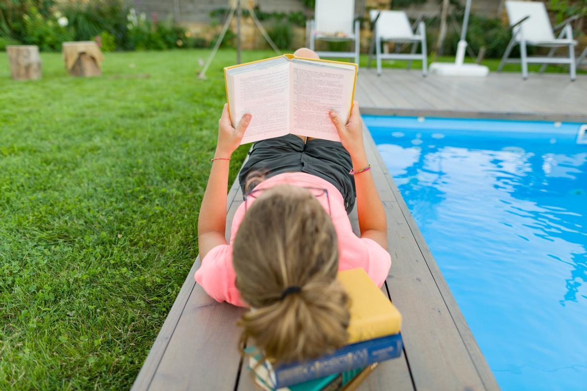 Una xiqueta llegint vora una piscina