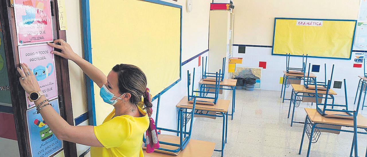 Una maestra cuelga unos carteles en la puerta de su clase con unas recomendaciones para hacer frente al covid.