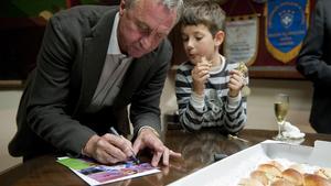 El seleccionador catalán Johan Cruyff firma un autógrafo supervisado por un niño mientras come unos canapés en la presentación de la selección catalana que jugará el día 30 ante Túnez .