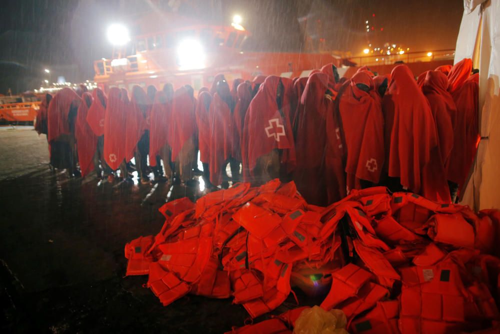 Migrants stand under the rain next to life-vests ...