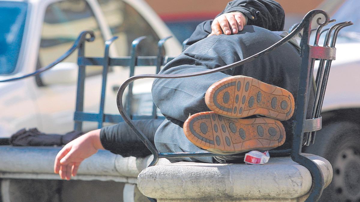 Un hombre duerme en un banco en plena calle.