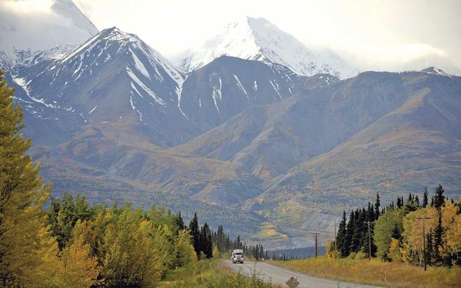 Eighteen wheeler or truck driving on a highway through snow-capped mountains and autumn or fall colours in Yukon, Canada