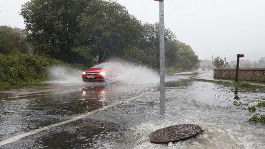 Un coche circula por una carretera llena de agua por las lluvias.