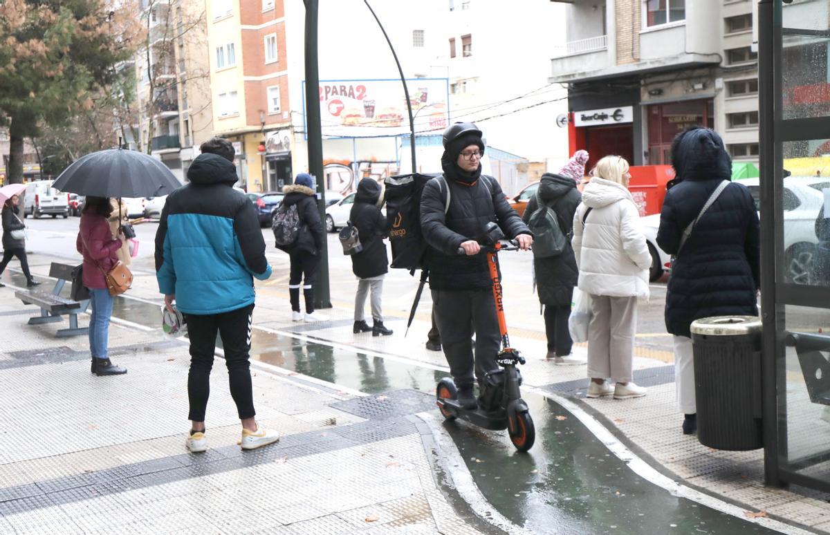 Un usuario de patinete esquiva a los viajeros del bus que esperan alrededor de la parada.