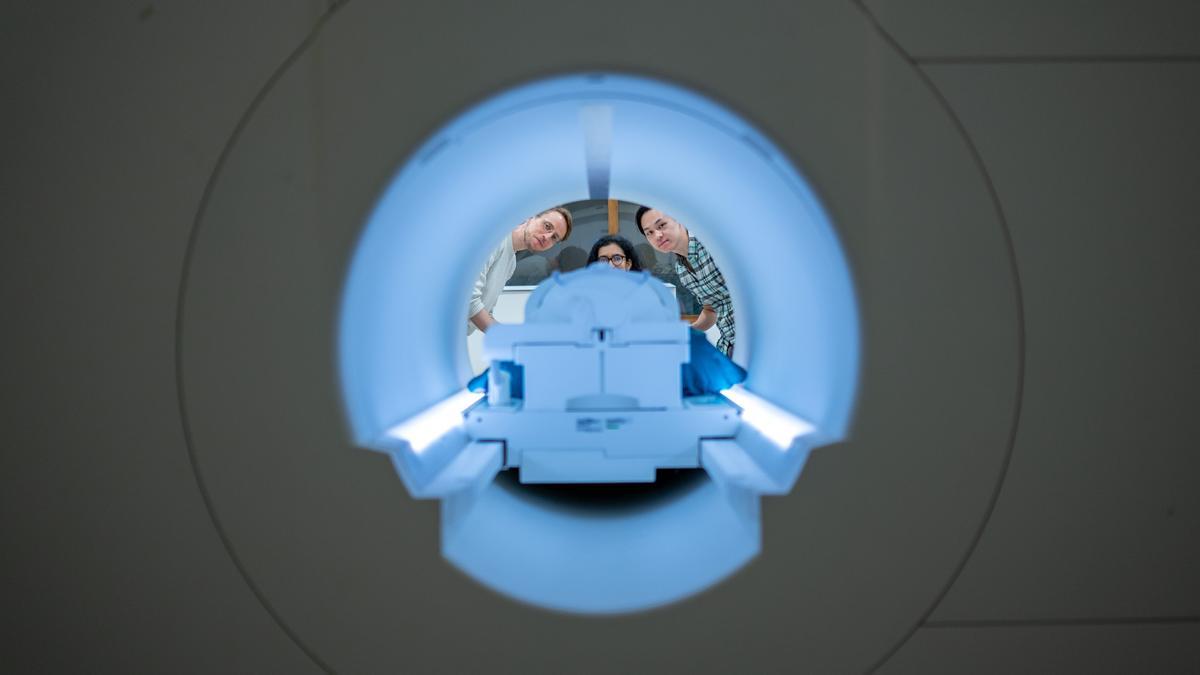Los investigadores Alex Huth, Jerry Tang y Shailee Jain posan junto a uno de los escáneres utilizados en este estudio.